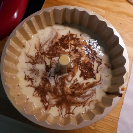 A bundt pan filled with white batter with brown swirls.